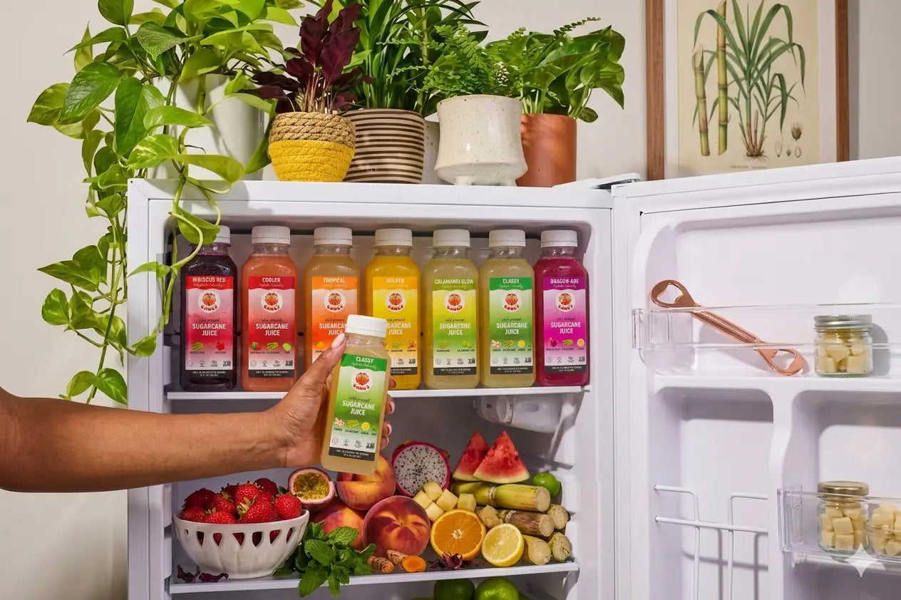 Open refrigerator with various drinks and fruits, person holding a juice box.