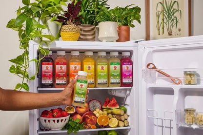 Open refrigerator with various drinks and fruits, person holding a juice box.