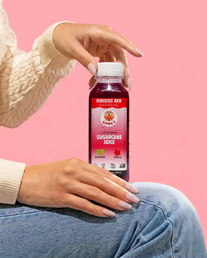 Person holding a bottle of HIBISCUS RED sugarcane juice against a pink background